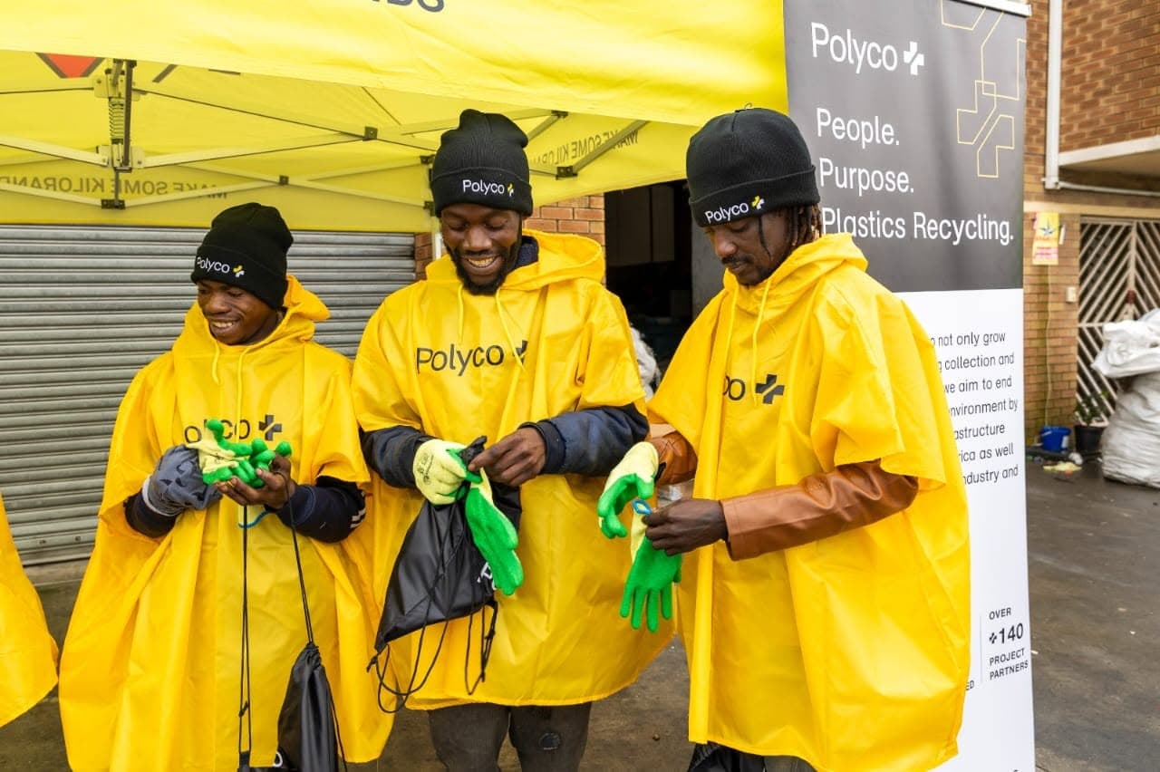 Three collectors in yellow Polyco ponchos putting on green gloves before a buyback day