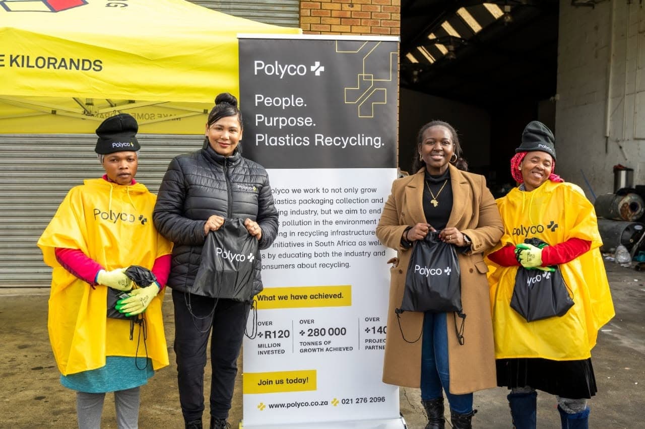 Four women holding Polyco drawstring bags in front of a Polyco ‘People. Purpose. Plastics Recycling.’ banner at a WasteGo Green buyback event