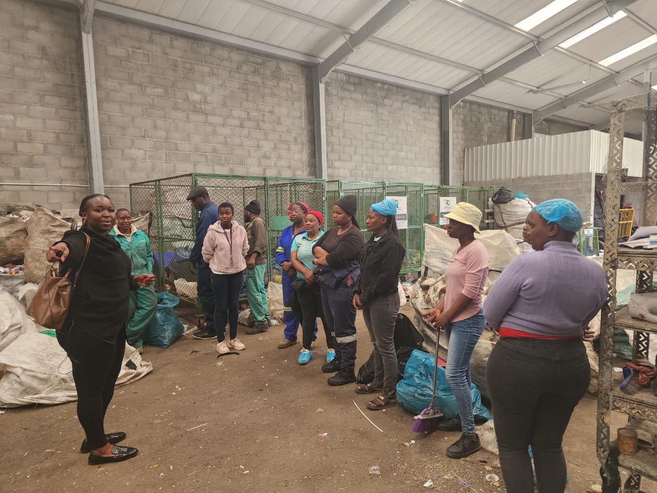 A manager briefing a group of mostly women workers among collection cages and bulk bags in the warehouse
